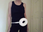 Person is shown wearing a Stoma-donut around the hips. This is a 5 by 7 inch foam donut about 2 inches thick, comes with an elastic strap for the waist. The center hole is 3 by 2 inches and protects a stoma from the pressure of a seat belt.